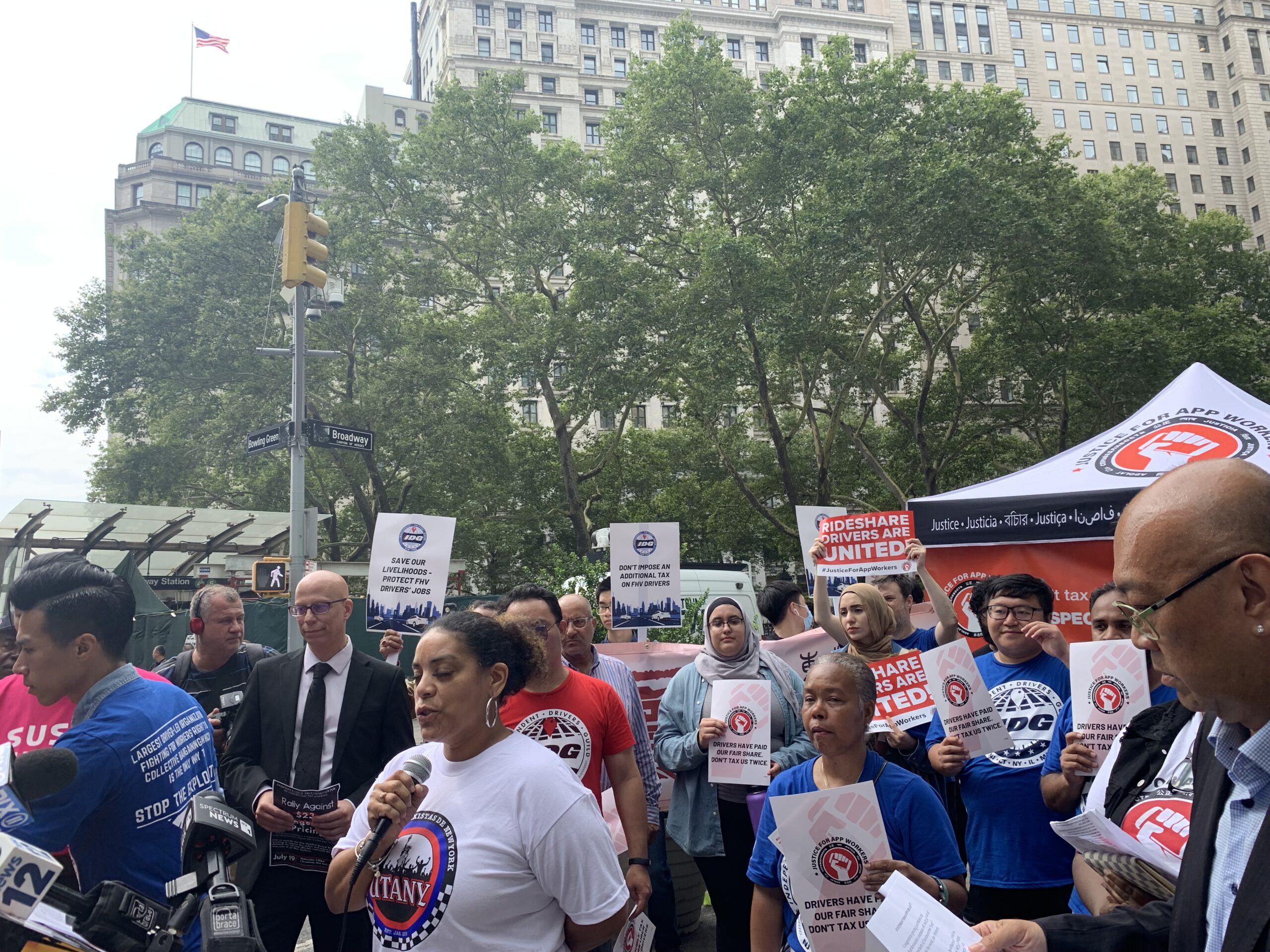 A group of around 30 people protest outdoors while holding signs. A tent is visible behind them.