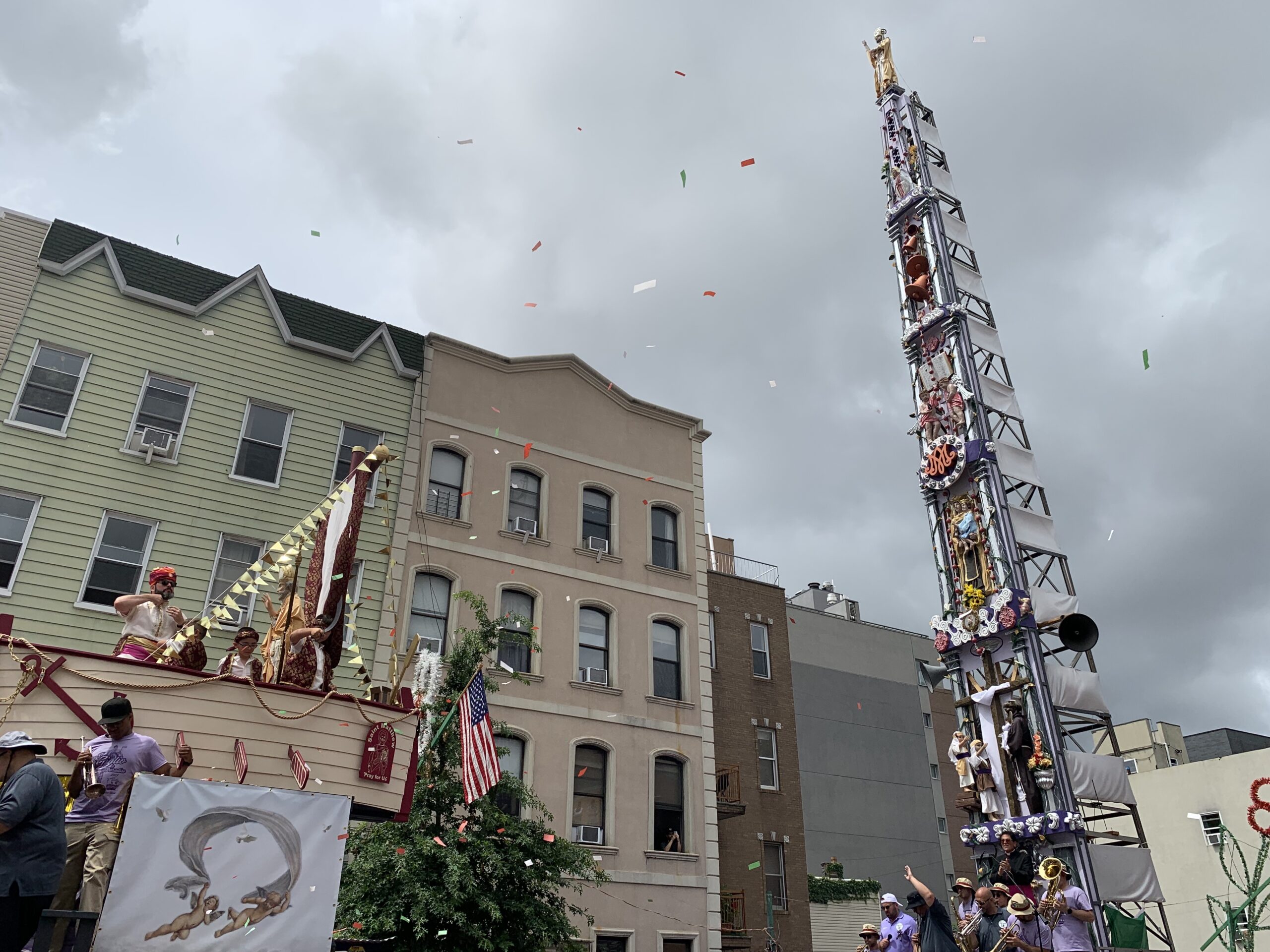 The Giglio stands over the crowd in front of a cloudy sky, facing another structure with a wooden boat on it.