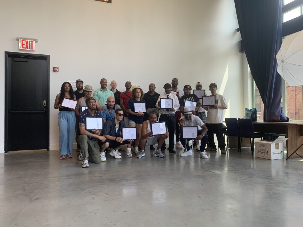 A group of around 20 people poses for a group photo during the graduation ceremony. Many of them hold white certificates in thin black frames.